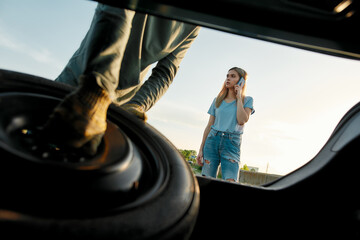 Wall Mural - Young woman calling car service or assistance while having troubles with her car, Close up of hands of man taking out spare wheel