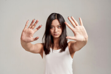 Portrait of young asian woman wearing white shirt having serious confident look while making stop gesture with two hands isolated over grey background