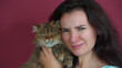 © Nicolaos - A cat with an angry funny face in the arms of a young beautiful mistress. The hostess parodies the evil face of her cat.