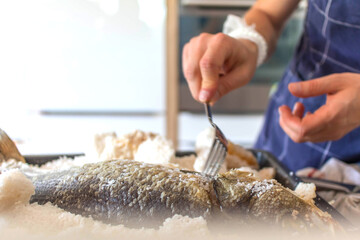 The chef prepares fresh sea bass fish, baked and covered with salt to serve. Preparing to cook fish food. Sea bass fish.