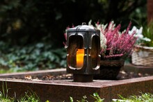 Grave Lantern Made Of Metal With Burning Candle In Front Of Grave Decoration In Blurred Background