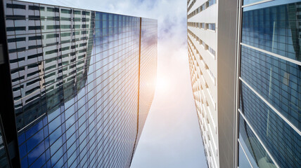 Bottom view of modern office buildings in the business district. Skyscraper glass facades on a bright sunny day with sunbeams in the blue sky.