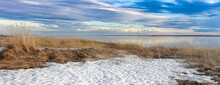 Sunset Spring Landscape With Sea And Sky In Blue Shades Snow Cover And Dry Grass.