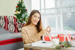© chinnarach - close up young asian woman try to put ribbon on wrapped gift box at living room with pine tree decoration for merry Christmas and happy new year festival season concept
