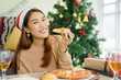 © chinnarach - close up young asian woman holing piece of Hawaiian flavor pizza and eating with happiness at living room for mini lunch meal before merry christmas celebration party for holiday lifestyle concept