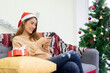 © chinnarach - close up young asian woman sitting on couch and using smartphone to checking event on social media or website or shopping online at home for christmas celebration festival concept