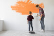 © Andrii Lysenko - mom and son are painting the wall with orange paint. home renovation concept