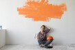 © Andrii Lysenko - happy woman sits on the floor with orange spot on the wall. home renovation concept