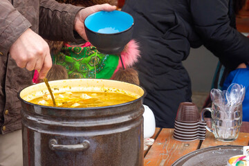 Put a ladle of soup from a large black enamel pan into a plate. Lunch in the open air in the yard.