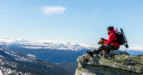 Man and dog standing on steep hillside and looking towards the snowy peaks of Jotunheimen in Norway. Staffordshire bullterrier, hiking, trekking, lifestyle, rondane and Norway concept.