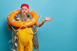 © wayhome.studio  - Horizontal shot of shocked embarrassed bearded male seafarer poses with inflated lifering fishing net smokes pipe raises hand over blue wall demonstrates copy space for your advertising content