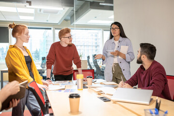 Poster - Young Asian female broker standing by table and explaining her point of view