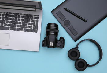 workspace of a photographer or retoucher. laptop, graphic tablet, camera and headphones on a blue ba