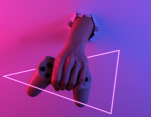 Wall Mural - Hand holds gamepad through torn hole. Creative pop art pink blue neon color. Trendy gradient illumination. Night light