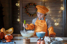 Cute Curly-haired Boy In An Orange Chef Costume Is Preparing Pumpkin Pie For Thanksgiving. Family Holiday Traditions