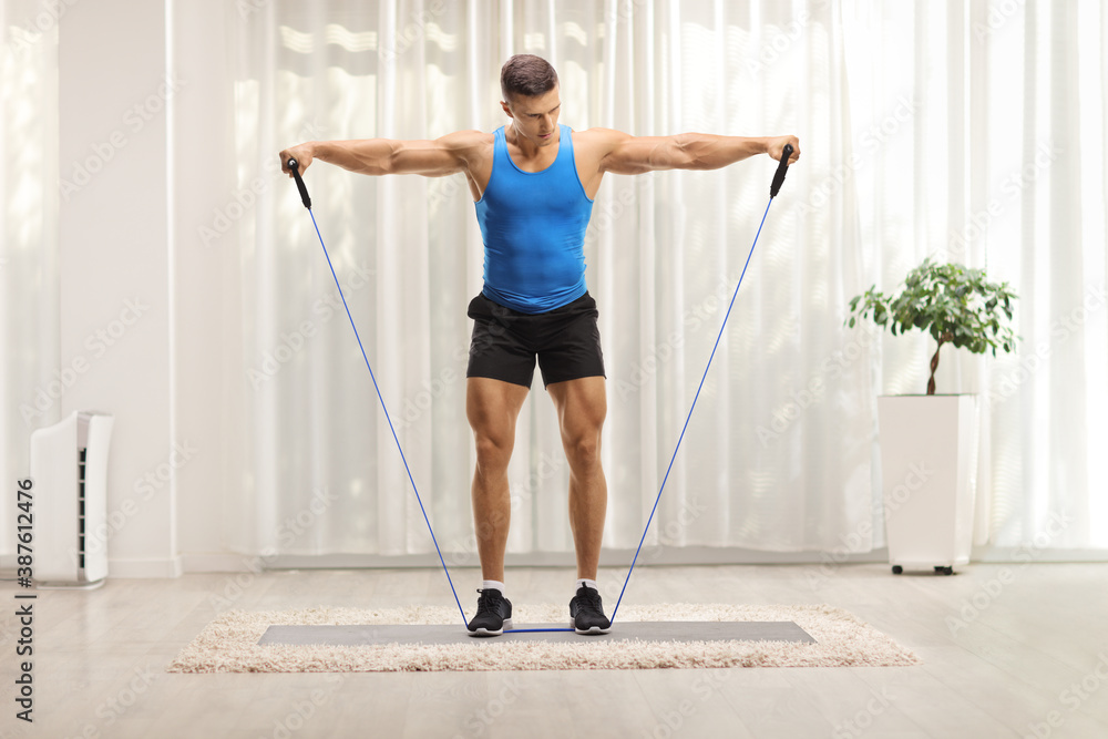 Full length hot of a muscular guy exercising with a resistance band at home - obrazy, fototapety, plakaty 