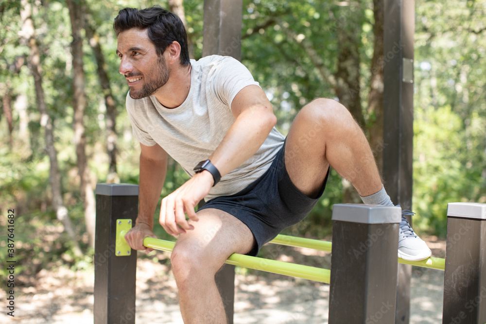 fit man doing exercises in forest outdoor gym using bars - obrazy, fototapety, plakaty 