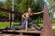 © Андрей Рыков - Mother and daughter stretching legs together on top of wooden staircase in public park on sunny summer morning. Family outdoor sports theme.