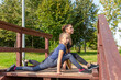 © Андрей Рыков - Mother and daughter stretching legs together on top of wooden staircase in public park on sunny summer morning. Family outdoor sports theme.