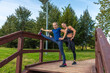 © Андрей Рыков - Mother and daughter stretching legs together on top of wooden staircase in public park on sunny summer morning. Family outdoor sports theme.