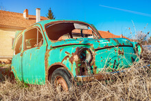 Rusty And Abandoned Retro Fiat 600 Car In A Junk Yard Against Clear Blue Sky In The Background. Old Wrecked Small European Car Left On The Field. 