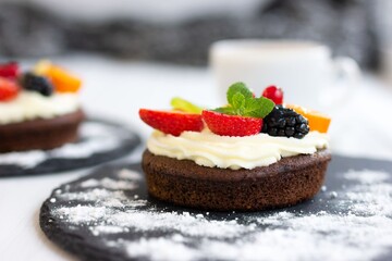 Chocolate cupcakes with cream cheese, fruits and berries. Biscuit mini cake with custard cream as coffee dessert. Close-up, side view