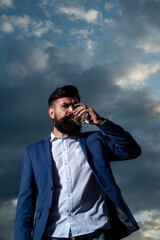 Man with beard and mustache holds alcoholic beverage on sky background. Service and alcoholism concept.