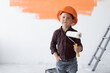 © Andrii Lysenko - a little boy dressed in an orange safety helmet holds a roller in his hands.