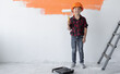 © Andrii Lysenko - a little boy dressed in an orange safety helmet holds a roller in his hands. Home renovation concept.