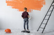 © Andrii Lysenko - a boy stands near the wall and paints it orange. Helping parents.