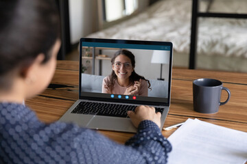 Canvas Print - Rear view of female worker talk speak chat on video call on laptop with smiling colleague coworker. Women employees have webcam digital conference on computer, brainstorm on online meeting at home.