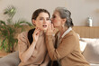 © ty - Happy middle mother whispering secret to her smiling daughter at home, gossiping, sharing secret. Beautiful woman hearing good news from mature mum, trusted relations.