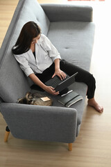 Wall Mural - Over head shot of happy young woman sitting on sofa and using tablet in living room.