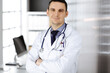 © cameravit - Male doctor standing straight with arms crossed in clinic near his working place. Perfect medical service in hospital. Medicine and healthcare concept