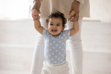 Wall Mural - cute little african american baby hold mom hands make first steps at home. small biracial toddler ch