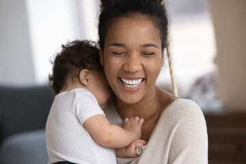 Wall Mural - Close up of overjoyed young african American mom hold hug little biracial infant baby daughter. Smiling ethnic mother embrace small toddler child show love care, play together. Motherhood concept.