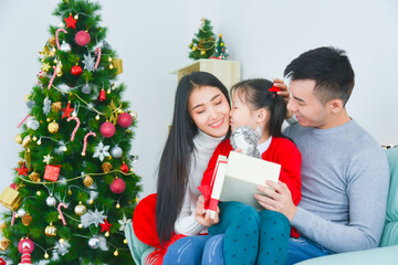 Wall Mural - Asian mom and dad opening gift box with her daughter. Near the Christmas tree at home. Little girl kissing her mother,thanks for present.