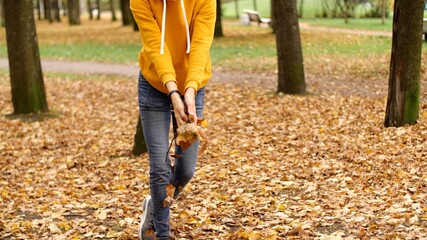 Legs in jeans and sneakers. Person in an autumn park throws up a yellow leaves. Walk in the autumn park. Hipster attractive adult woman in oversized yellow hoodie 