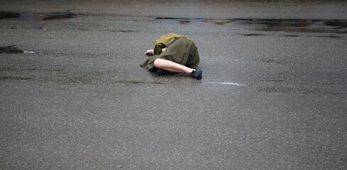 Young woman lying down on ground. Sick or ill girl unconscious outside on the wet asphalt. Victim of force abuse. A crime. Concept image