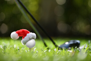 Festive-looking golf ball on tee with Santa Claus' hat on top for holiday season on golf course background..