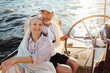 © Artem Varnitsin - Smiling mature woman looking at camera while her husband steering a sailboat. Two senior people enjoying a vacation on yacht.