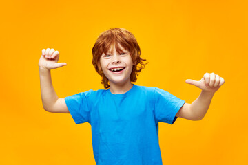 Cheerful boy with red hair shows his thumbs on yellow isolated background 