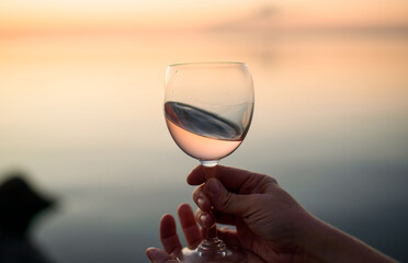 A beautiful glass with pink wine in the hands of a young girl. A glass of wine at sunrise. Romantic breakfast