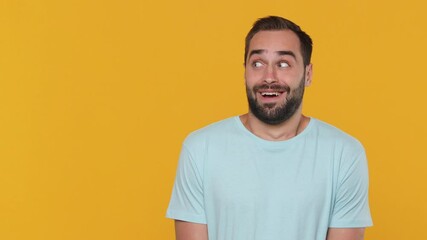 Wall Mural - Fun shocked surprised young man 20s years old in basic casual blue t-shirt looking camera and aside pointing on copy space workspace area isolated on yellow background studio. People lifestyle concept