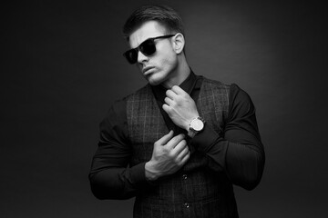 Wall Mural - Black and white portrait of beautyful guy on dark background. High fashion model posing in studio. Attractive man in classic suit and sunglasses.