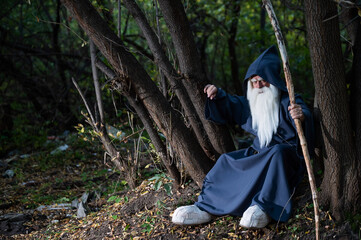 A wizard with a long gray beard and a cloak in a deep forest. An elderly man in a witcher costume