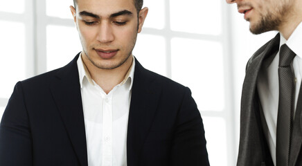 Two businessmen or partners working with tablet computer at the desk in modern office. Headshot of arab male entrepreneur or manager with colleague at workplace. Multi ethnic teamwork, partnership and