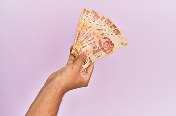 Hispanic hand holding 100 mexican pesos  banknotes over isolated pink background.