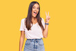 © Krakenimages.com - Young hispanic woman wearing casual white tshirt smiling with happy face winking at the camera doing victory sign with fingers. number two.