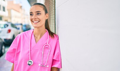 Wall Mural - Young hispanic doctor woman smiling happy leaning on the wall at street of city.